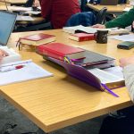 A close up of a table shared by students on which there are Bibles, a laptop, prayer books and notepads.