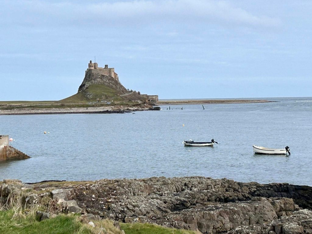 A view of Lindisfarne Castle with the sea and two boats in the foreground.