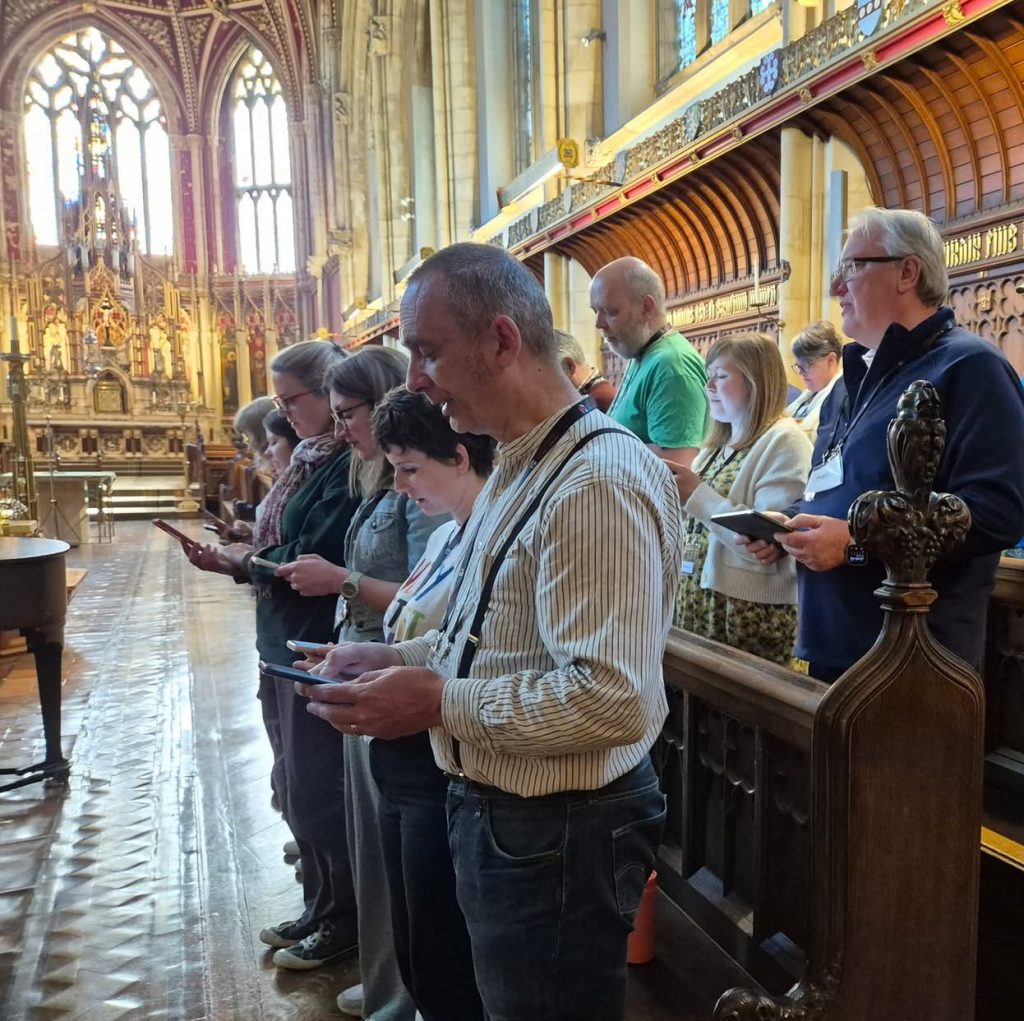 Staff and students stand in pews in a chapel, worshipping together. 